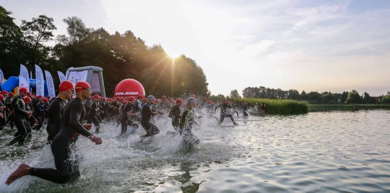 triathloniści podczas traithlon polska wbiegają grupowo do wody aby zwyciężyć w wyścigu